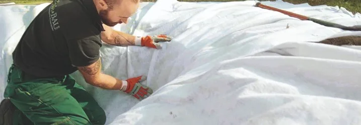 Person breitet weiße Plane auf Rasen aus